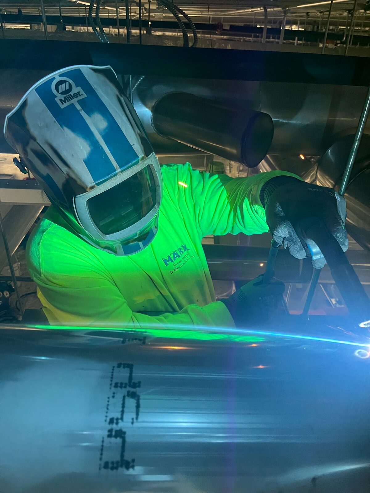 A sheet metal worker in protective gear welding a seam
